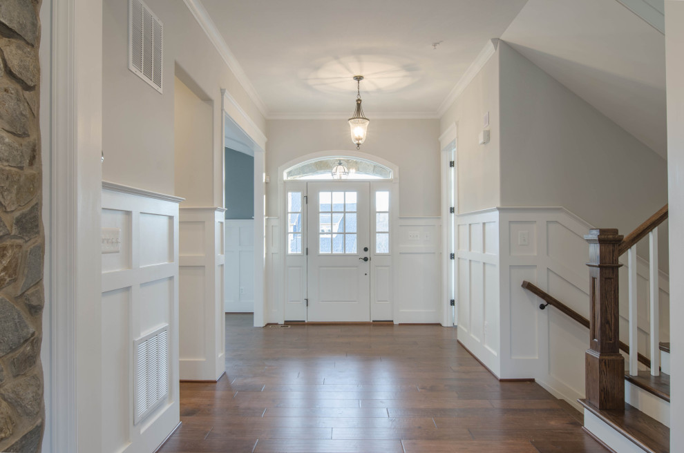На фото: фойе в классическом стиле с паркетным полом среднего тона, одностворчатой входной дверью, белой входной дверью, коричневым полом и панелями на стенах