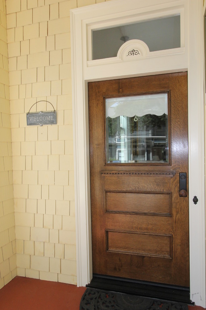 Immagine di una porta d'ingresso vittoriana con pareti gialle, pavimento in legno verniciato, una porta singola, una porta in legno bruno e pavimento rosso
