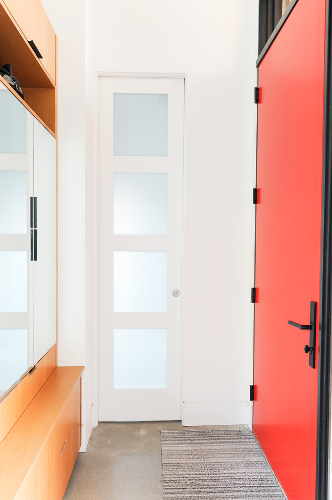 Immagine di una piccola porta d'ingresso moderna con pareti bianche, pavimento in cemento, una porta singola, una porta rossa e pavimento grigio