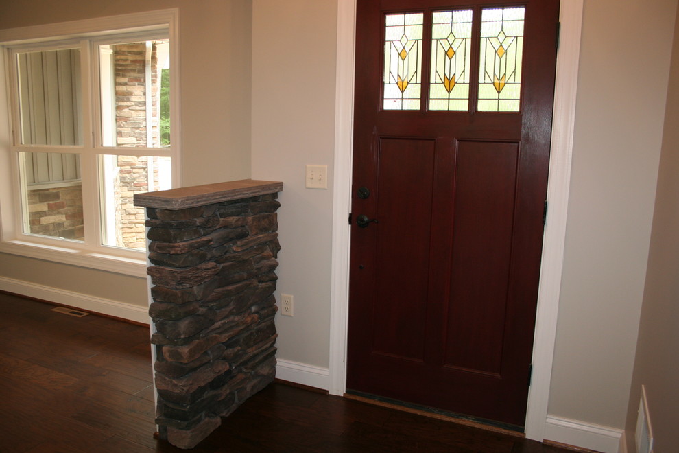 Cette image montre une grande porte d'entrée craftsman avec un mur gris, parquet foncé, une porte simple, une porte en bois foncé et un sol marron.