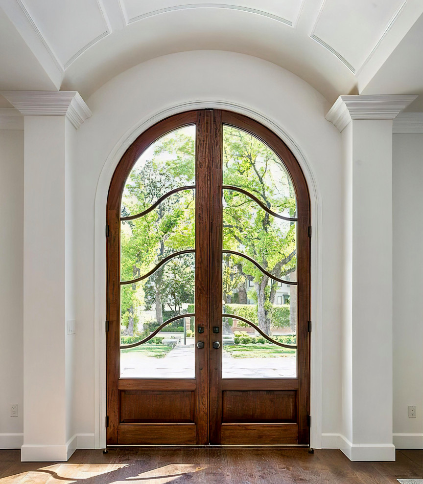 Cette photo montre une très grande porte d'entrée avec un mur blanc, un sol en bois brun, une porte double, une porte en bois brun, un sol marron et un plafond voûté.