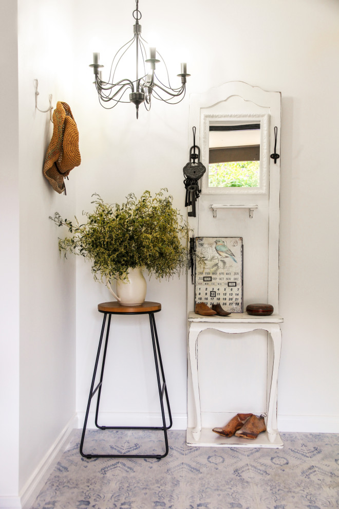 Shabby chic-inspirerad inredning av en entré, med vita väggar och flerfärgat golv