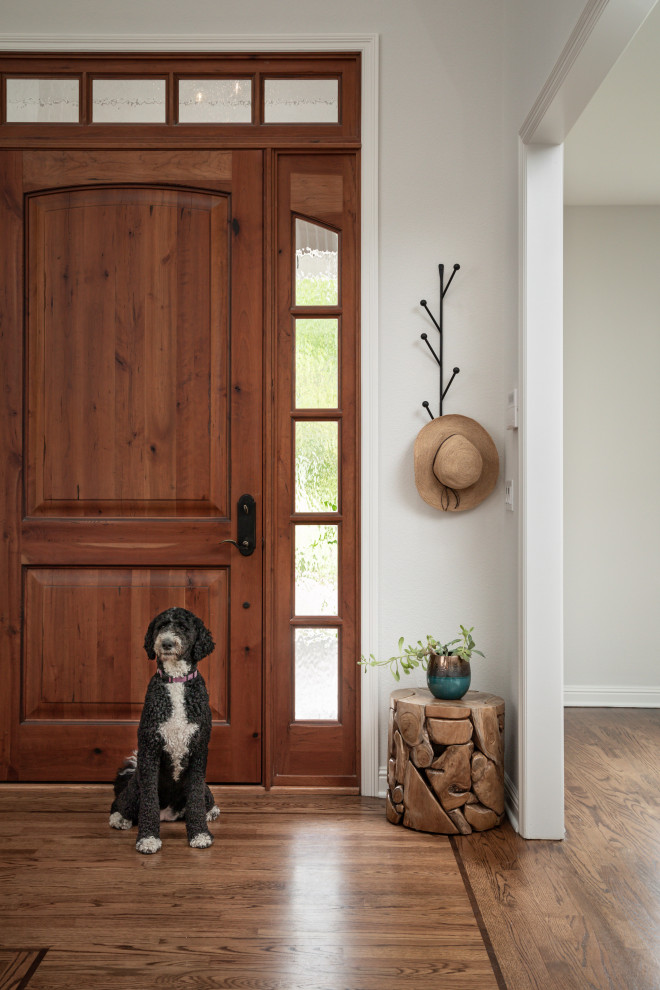 Cette image montre une grande porte d'entrée traditionnelle avec un mur blanc, un sol en bois brun, une porte simple, une porte en bois brun et un sol marron.