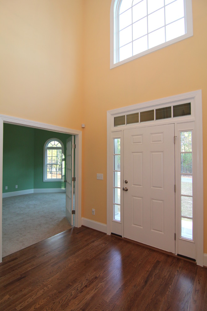 Immagine di un grande ingresso classico con pareti gialle, parquet scuro, una porta singola e una porta bianca