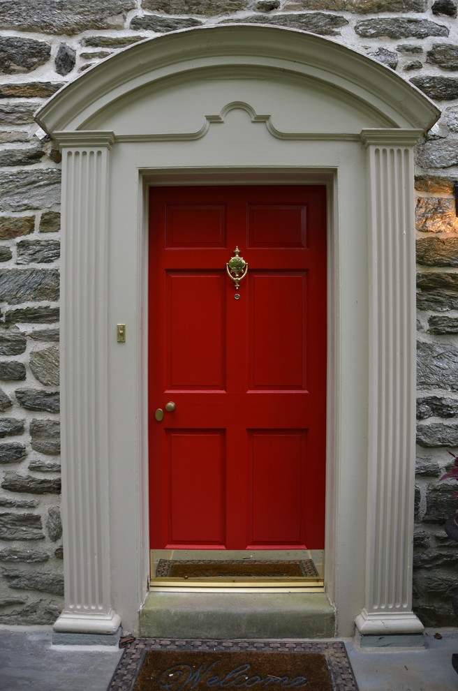 Cette image montre une petite porte d'entrée traditionnelle avec une porte simple et une porte rouge.