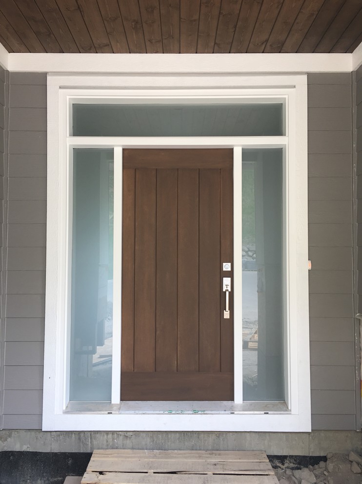Réalisation d'une porte d'entrée champêtre avec un mur gris, sol en béton ciré, une porte simple, une porte en bois brun et un sol gris.