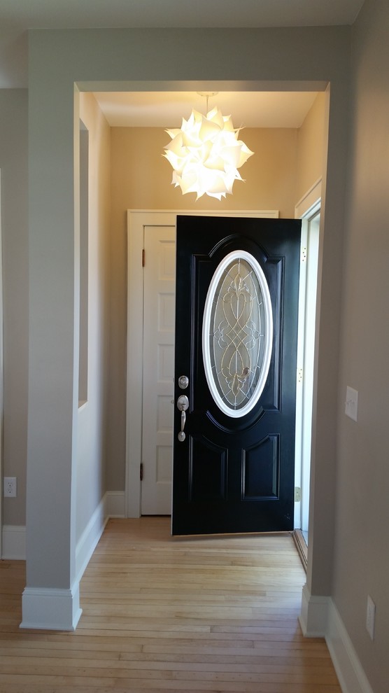 Modern inredning av en entré, med ljust trägolv och en svart dörr