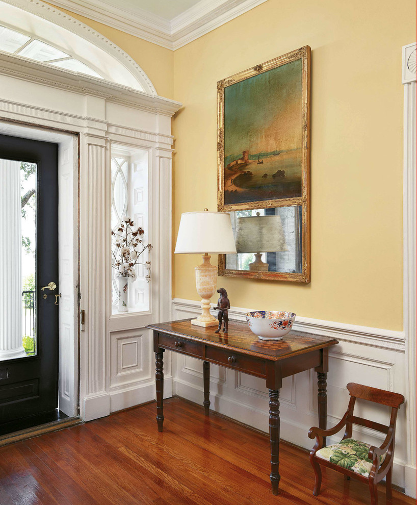 Großer Klassischer Eingang mit gelber Wandfarbe, braunem Holzboden, Einzeltür und schwarzer Haustür in Charleston