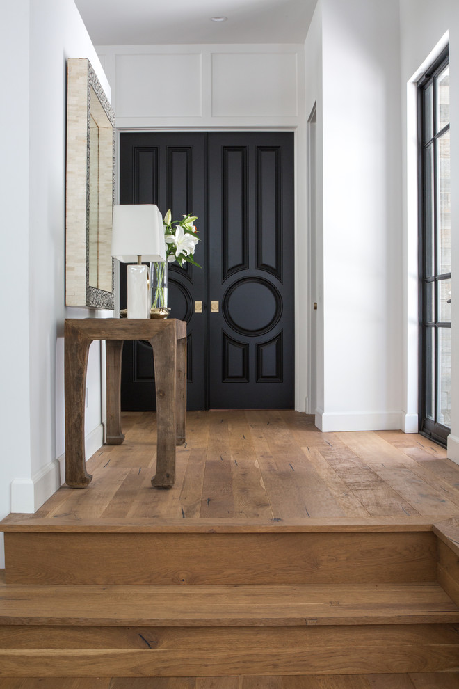 Diseño de entrada clásica renovada con paredes blancas, suelo de madera en tonos medios, puerta doble, puerta negra y suelo marrón
