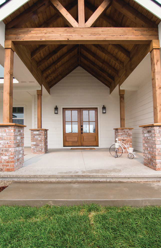 Diseño de puerta principal de estilo de casa de campo grande con paredes blancas, suelo de cemento, puerta doble y puerta de madera en tonos medios