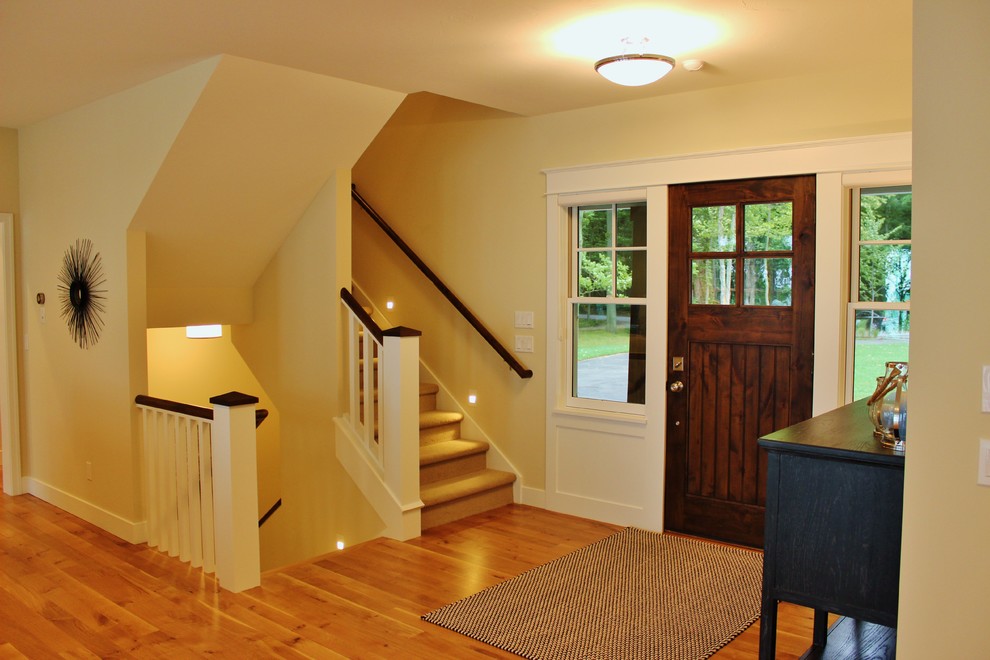 Imagen de puerta principal costera con paredes beige, suelo de madera en tonos medios, puerta simple y puerta de madera oscura