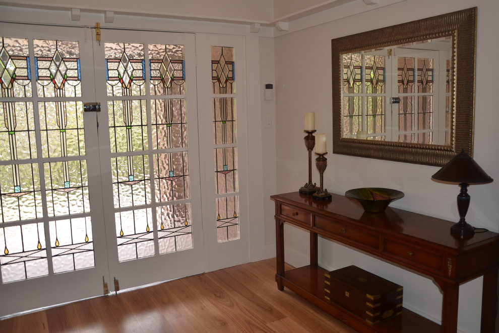 На фото: фойе в стиле неоклассика (современная классика) с белыми стенами, полом из фанеры, двустворчатой входной дверью, белой входной дверью и коричневым полом с