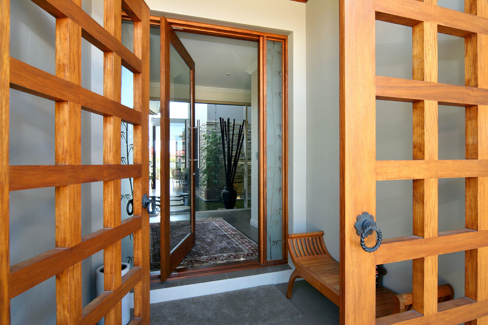 Foto di un ingresso o corridoio etnico con pareti beige, pavimento con piastrelle in ceramica, una porta a pivot, una porta in legno chiaro e pavimento grigio