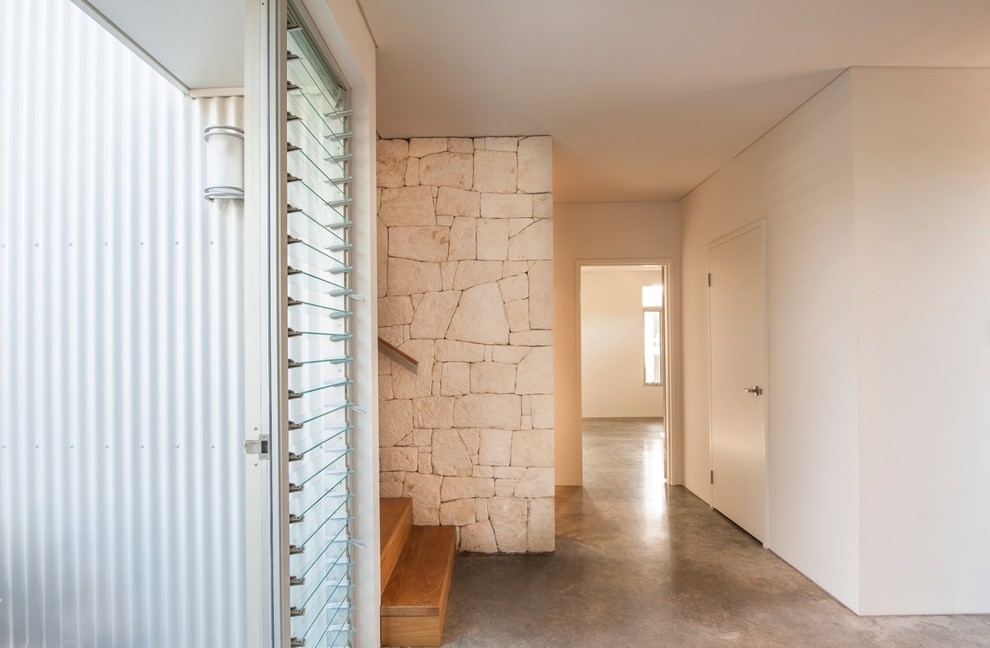 На фото: маленькая прихожая в современном стиле с бетонным полом, поворотной входной дверью и входной дверью из дерева среднего тона для на участке и в саду