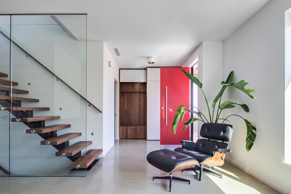 Ispirazione per un corridoio contemporaneo con pareti bianche, pavimento in cemento, una porta singola, una porta rossa e pavimento grigio