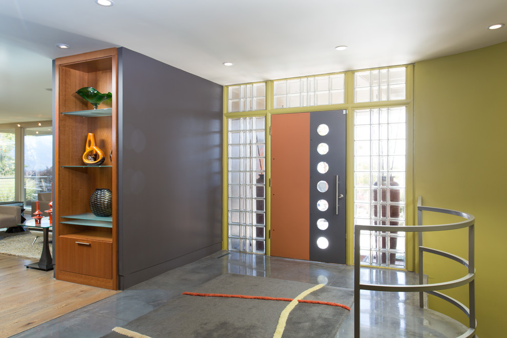 60 tals inredning av en mellanstor ingång och ytterdörr, med grå väggar, betonggolv, en enkeldörr, en orange dörr och grått golv