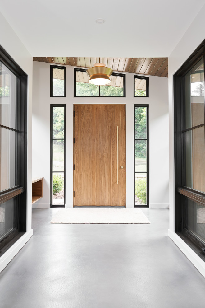 グランドラピッズにあるラグジュアリーな巨大なモダンスタイルのおしゃれな玄関ドア (コンクリートの床、淡色木目調のドア、グレーの床) の写真