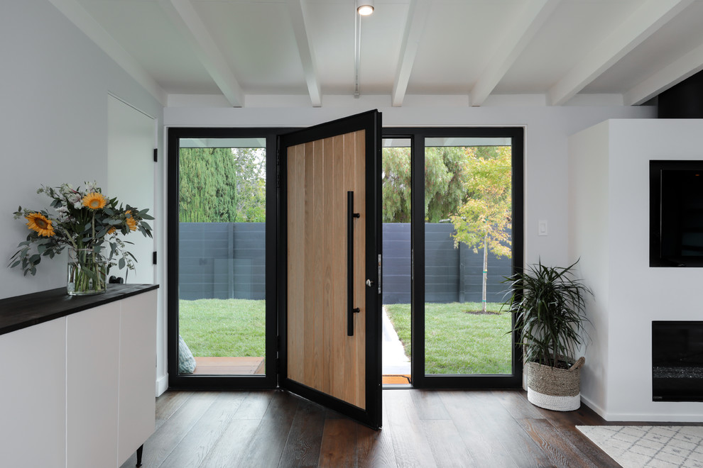 Foto di una porta d'ingresso minimalista di medie dimensioni con pareti bianche, parquet scuro, una porta a pivot, una porta in legno chiaro e pavimento marrone