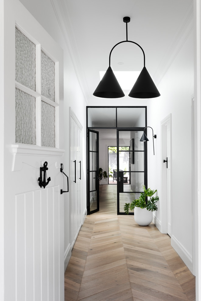 Modern inredning av en ingång och ytterdörr, med vita väggar, mellanmörkt trägolv, en enkeldörr, en vit dörr och brunt golv