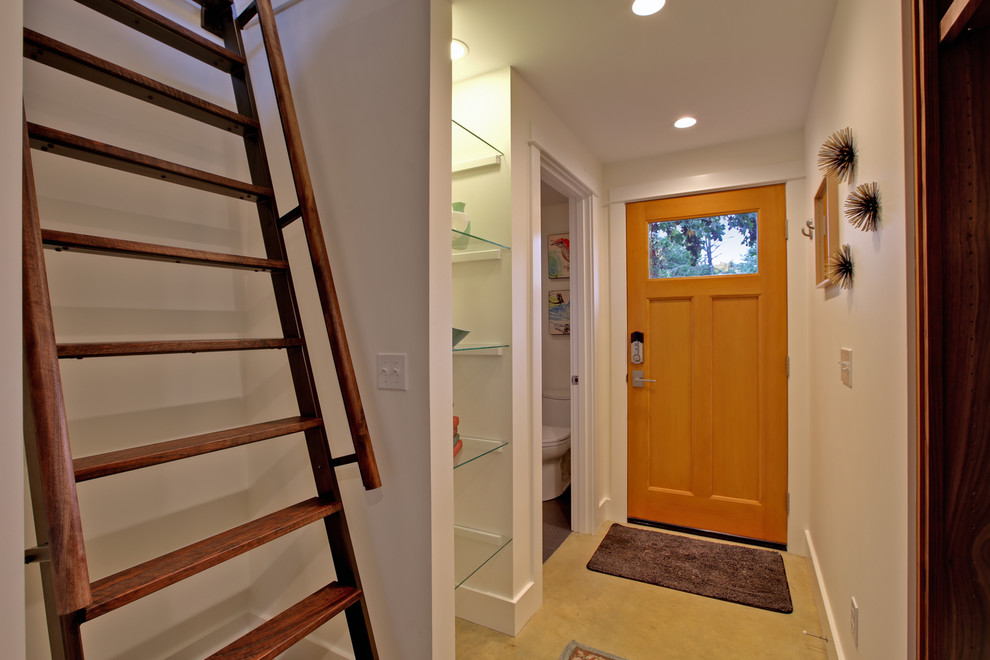 Пример оригинального дизайна: маленькая входная дверь в стиле неоклассика (современная классика) с белыми стенами, бетонным полом, одностворчатой входной дверью и входной дверью из светлого дерева для на участке и в саду