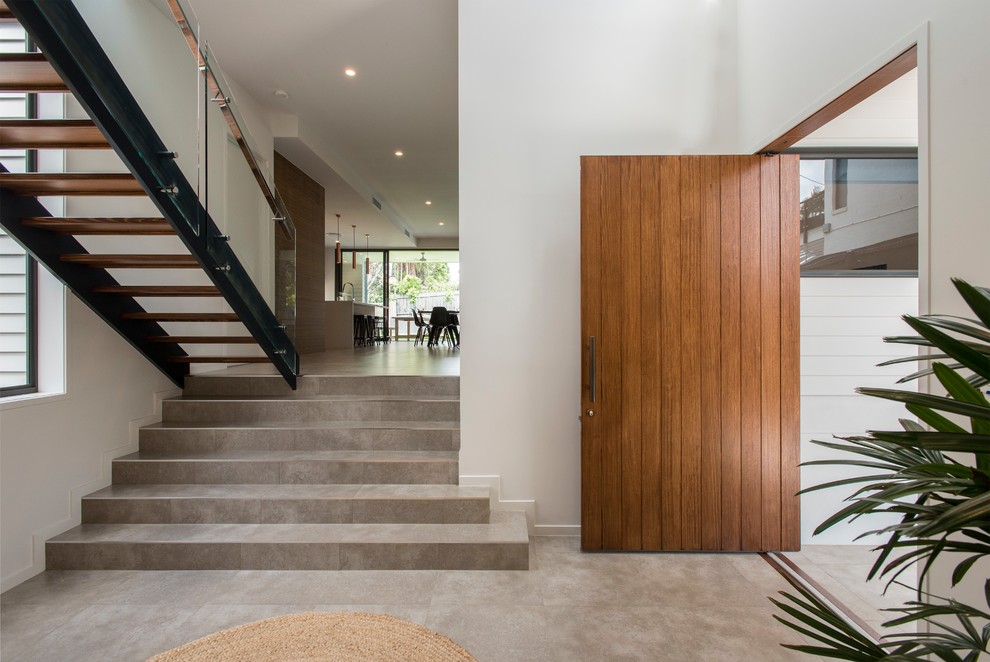 Immagine di un ingresso contemporaneo con pareti bianche, pavimento con piastrelle in ceramica, una porta a pivot, una porta in legno bruno e pavimento grigio