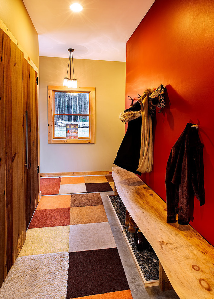 バーリントンにある高級な広いラスティックスタイルのおしゃれな玄関ロビー (赤い壁、コンクリートの床、グレーの床、白いドア) の写真