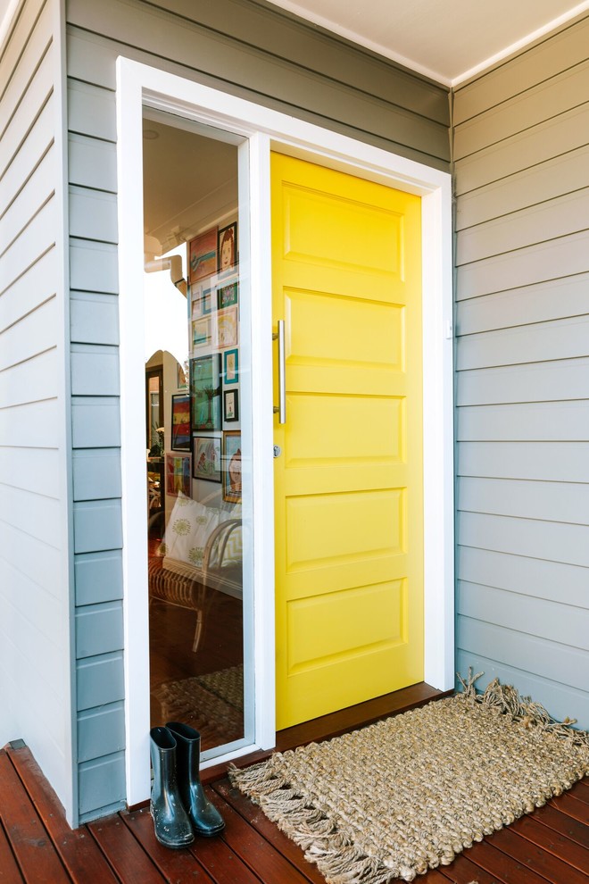 Foto på en funkis ingång och ytterdörr, med blå väggar, mellanmörkt trägolv, en enkeldörr, en gul dörr och brunt golv
