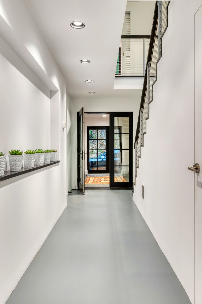 Diseño de hall moderno con paredes blancas, suelo de cemento, puerta simple y puerta negra