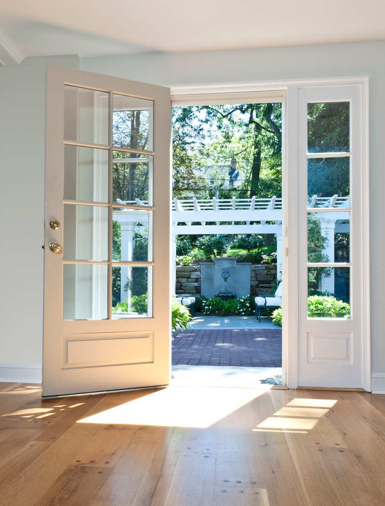 Cette image montre une porte d'entrée traditionnelle de taille moyenne avec un mur bleu, parquet clair, une porte simple, une porte en verre et un sol marron.