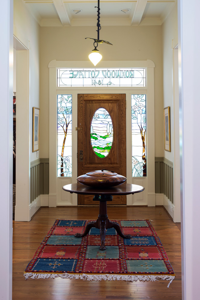 Cette image montre une porte d'entrée victorienne de taille moyenne avec un mur beige, un sol en bois brun, une porte simple et une porte en verre.