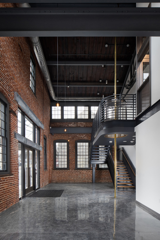 Immagine di un ampio ingresso o corridoio industriale con pavimento in laminato, una porta a due ante, una porta in vetro, pavimento grigio, travi a vista e pareti in mattoni