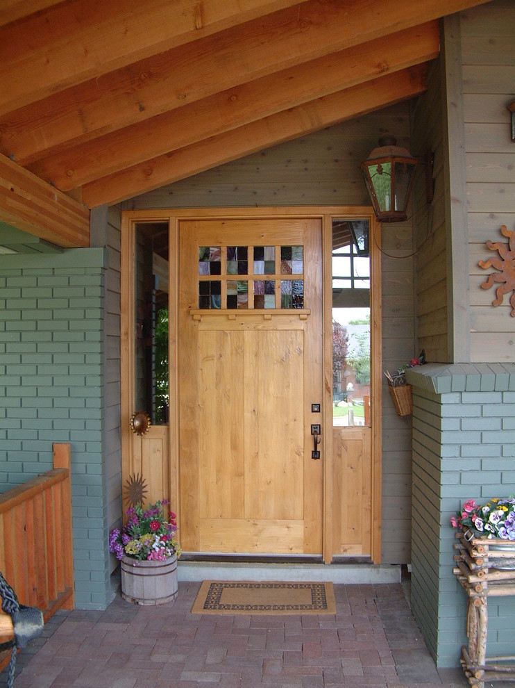 Cette image montre une porte d'entrée craftsman de taille moyenne avec un mur bleu, un sol en brique, une porte simple et une porte en bois clair.