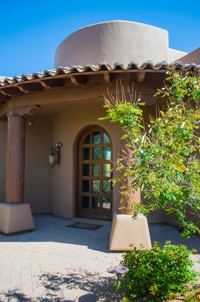 フェニックスにあるサンタフェスタイルのおしゃれな玄関ドア (ベージュの壁、レンガの床、木目調のドア、マルチカラーの床) の写真