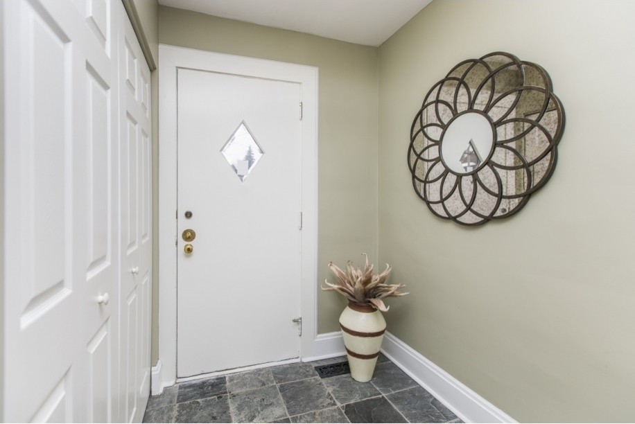 Cette photo montre une petite entrée chic avec un vestiaire, un mur vert, un sol en calcaire, une porte simple, une porte blanche et un sol noir.