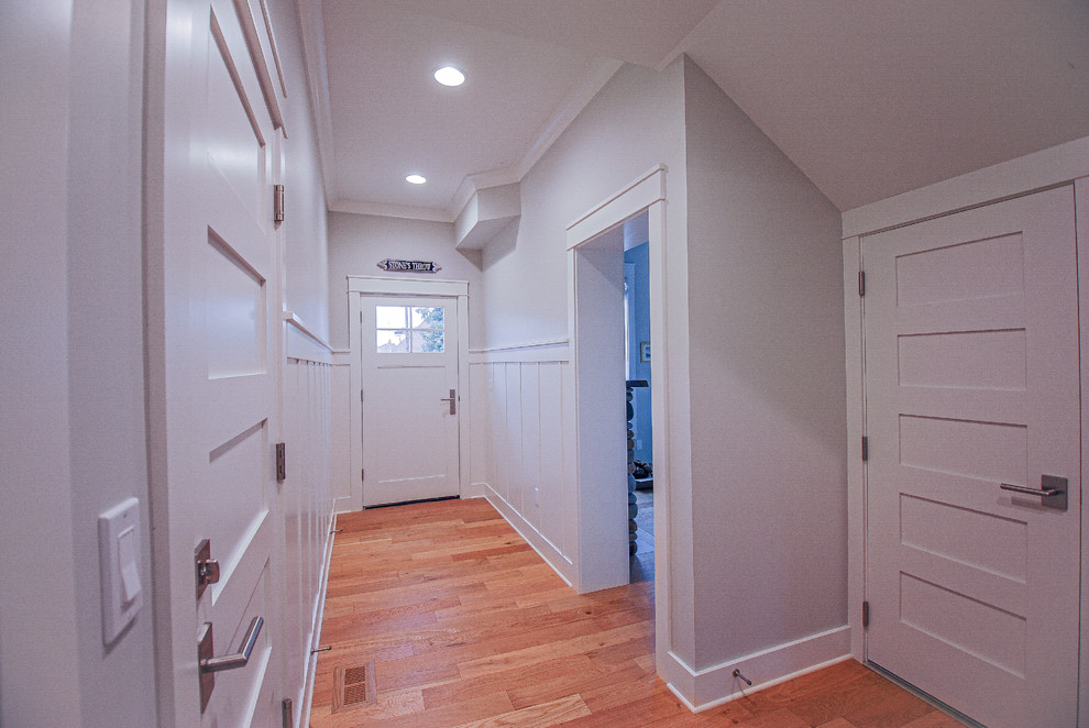 Modelo de hall tradicional grande con paredes blancas, suelo de madera en tonos medios, puerta simple y puerta blanca