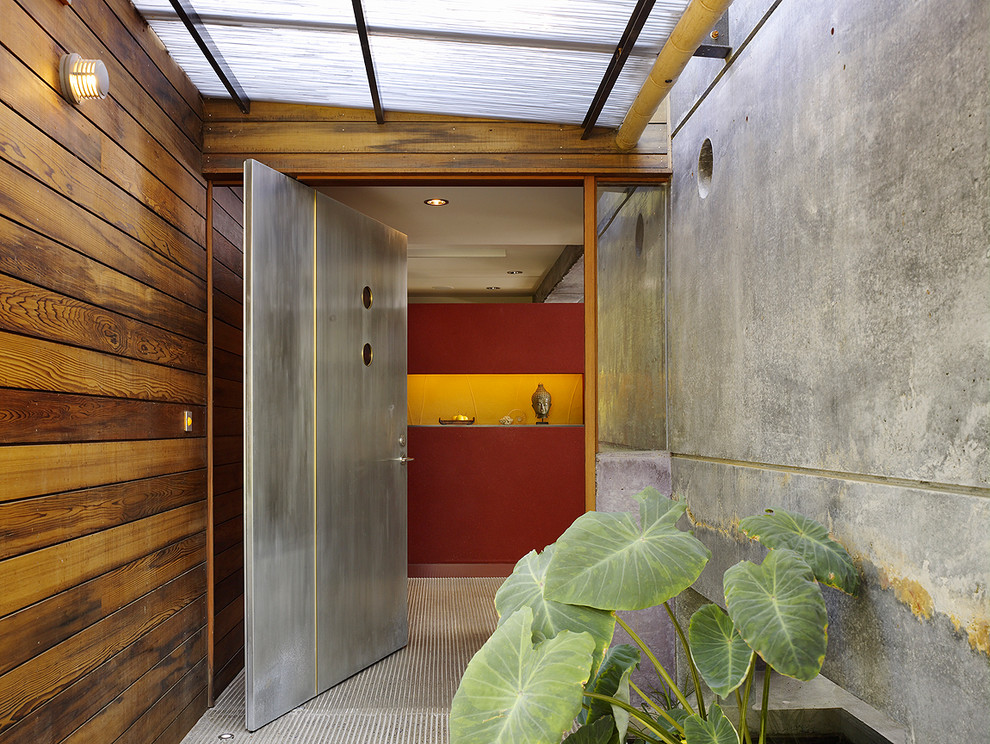 Cette photo montre une grande porte d'entrée tendance avec un mur rouge, sol en béton ciré, une porte pivot et une porte métallisée.