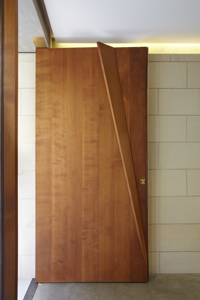 Réalisation d'une grande porte d'entrée minimaliste avec un mur beige, sol en béton ciré, une porte pivot et une porte en bois brun.