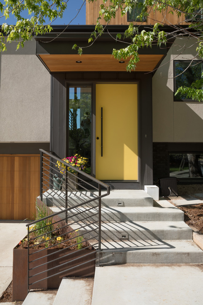 Modelo de puerta principal actual con paredes grises, suelo de cemento, puerta simple, puerta amarilla y suelo gris