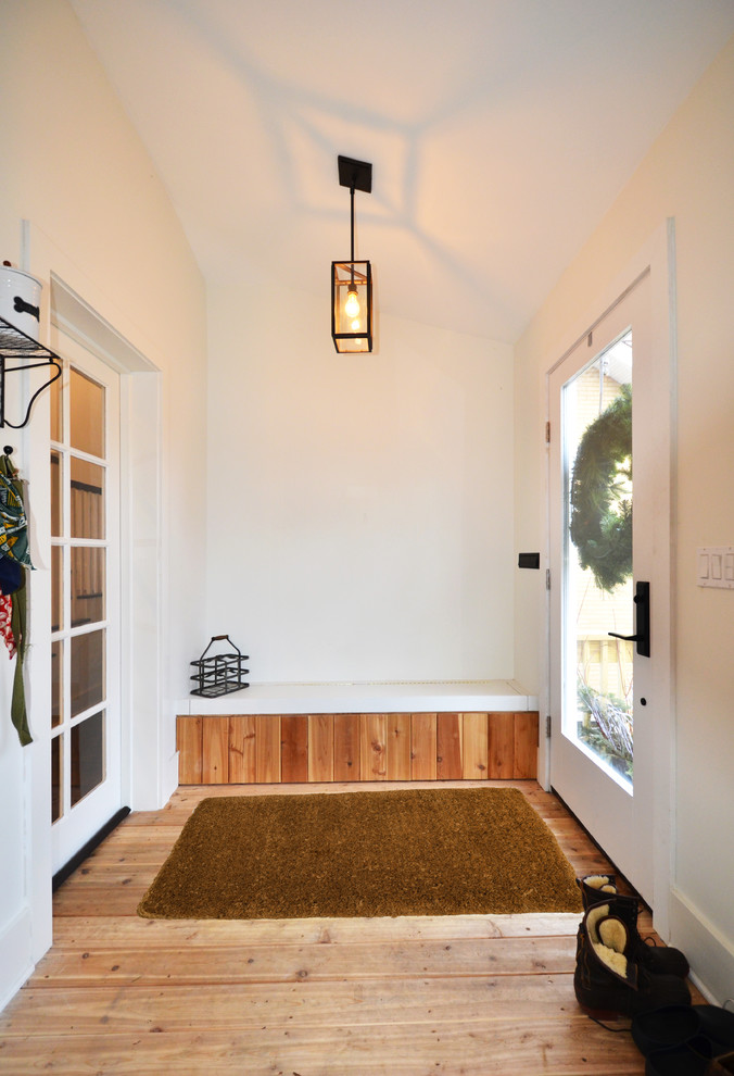 Réalisation d'une entrée champêtre de taille moyenne avec un vestiaire, un mur blanc, parquet clair, une porte pivot, une porte blanche et un sol marron.