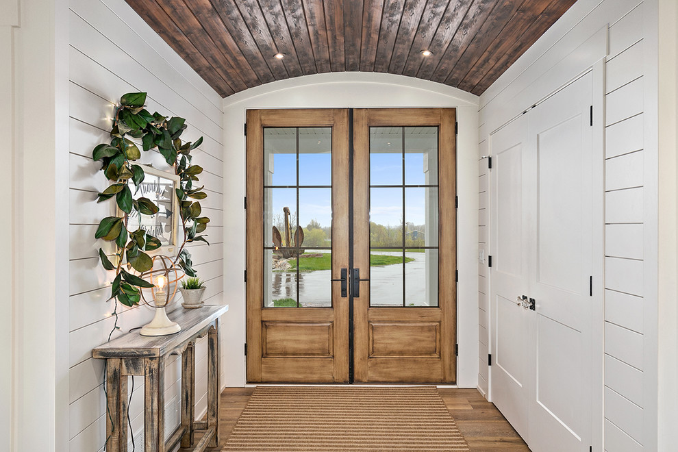 На фото: входная дверь в стиле кантри с белыми стенами, двустворчатой входной дверью, коричневым полом и стеклянной входной дверью