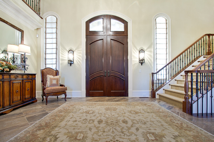 Пример оригинального дизайна: огромное фойе в классическом стиле с бежевыми стенами, полом из травертина, двустворчатой входной дверью и входной дверью из темного дерева