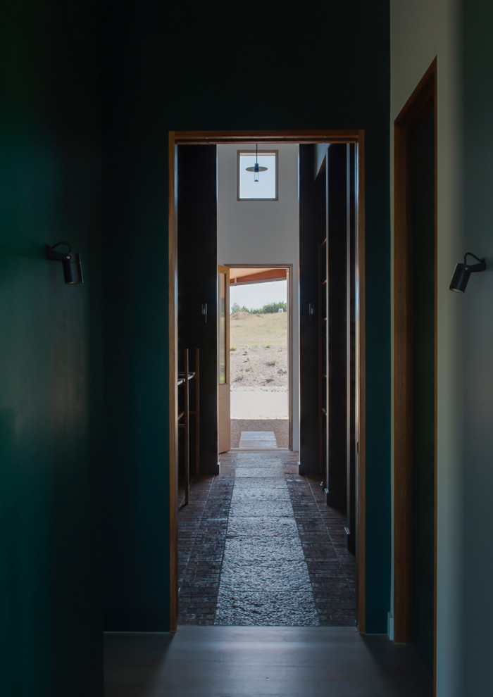 Réalisation d'une grande entrée minimaliste avec un couloir, un mur marron, un sol en brique, une porte simple, une porte en bois brun et un sol marron.
