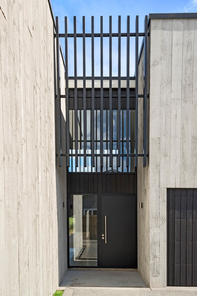 Immagine di una grande porta d'ingresso minimal con pareti grigie, pavimento in cemento, una porta singola, una porta nera e pavimento grigio