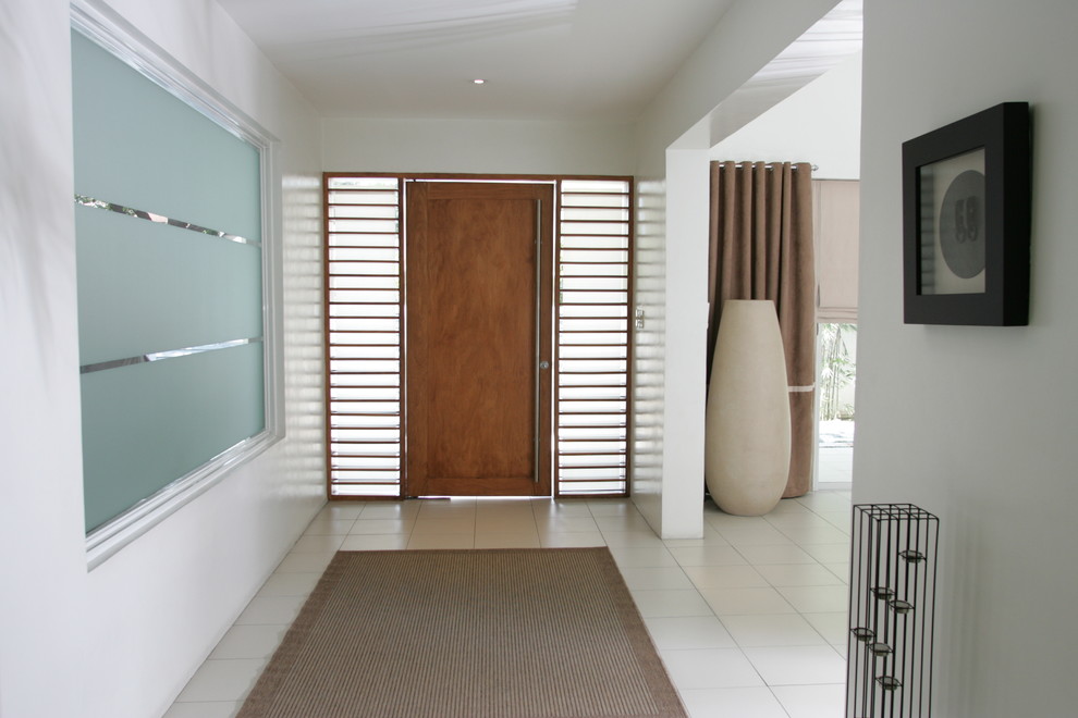 На фото: узкая прихожая в современном стиле с белыми стенами и входной дверью из дерева среднего тона с