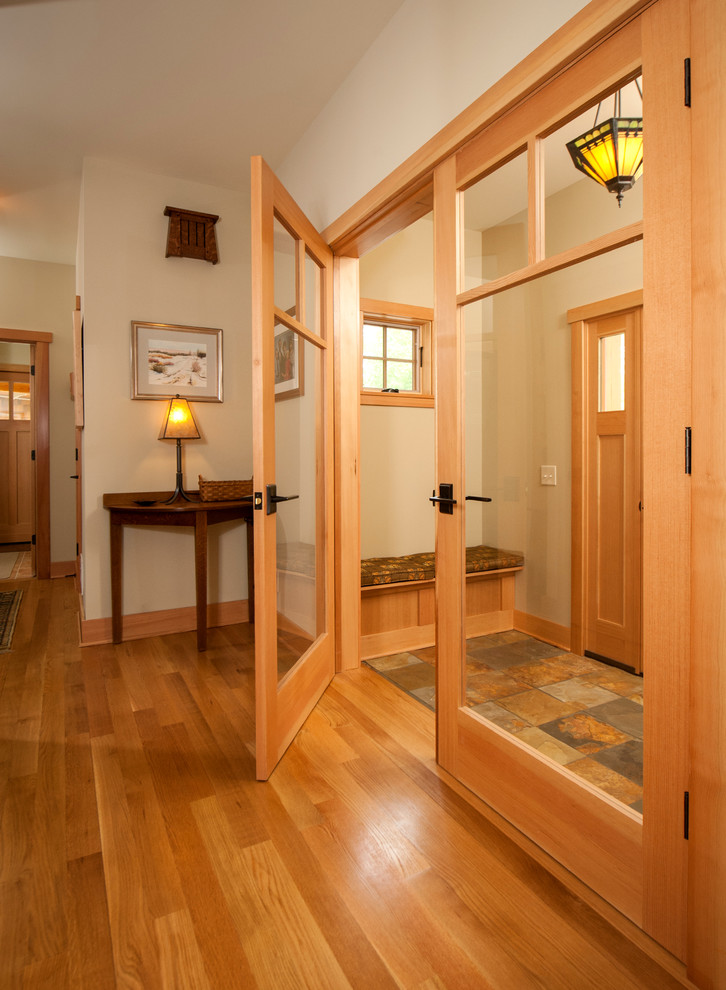 Cette image montre un vestibule craftsman de taille moyenne avec un mur beige, un sol en ardoise, une porte simple et une porte en bois clair.