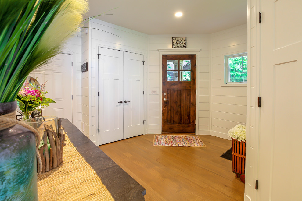 グランドラピッズにあるカントリー風のおしゃれな玄関 (白い壁、無垢フローリング、濃色木目調のドア) の写真