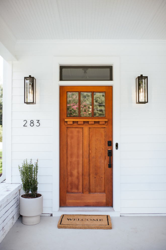 Imagen de puerta principal campestre con paredes blancas, suelo de cemento, puerta simple, puerta de madera en tonos medios y suelo gris