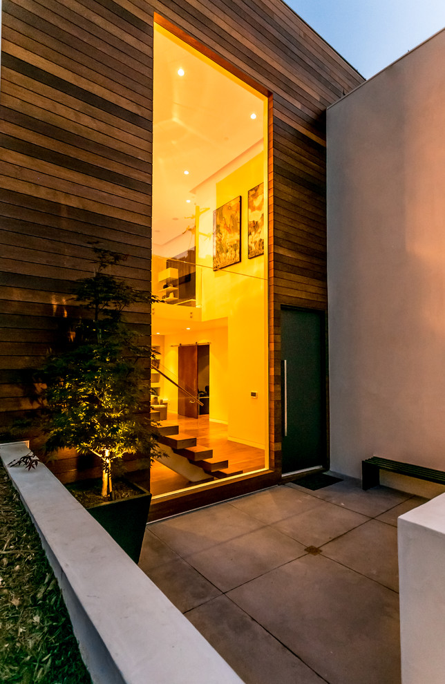 Medium sized modern front door in Los Angeles with brown walls, concrete flooring, a pivot front door and a black front door.