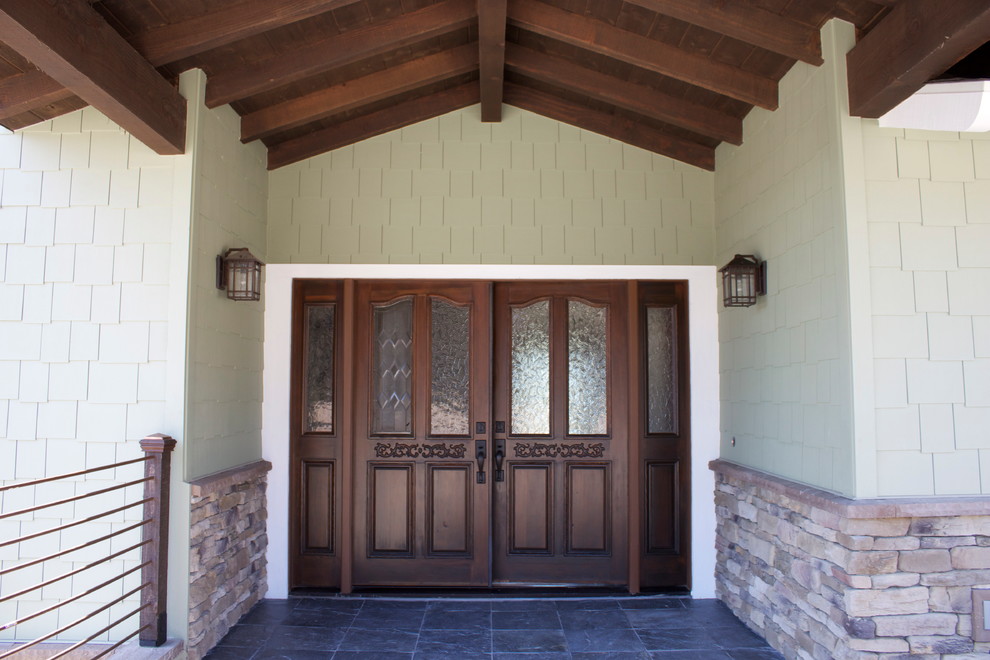 Aménagement d'une grande porte d'entrée craftsman avec un mur vert, un sol en ardoise, une porte double, une porte en bois foncé et un sol gris.