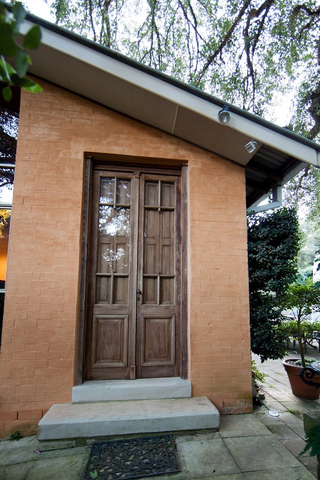 Cette image montre une porte d'entrée rustique de taille moyenne avec un mur orange, sol en béton ciré, une porte simple et une porte en bois foncé.